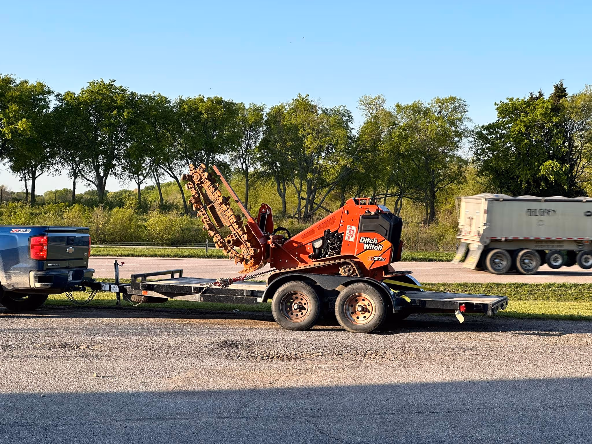 A mini skid steer with trencher attachment on a trailer